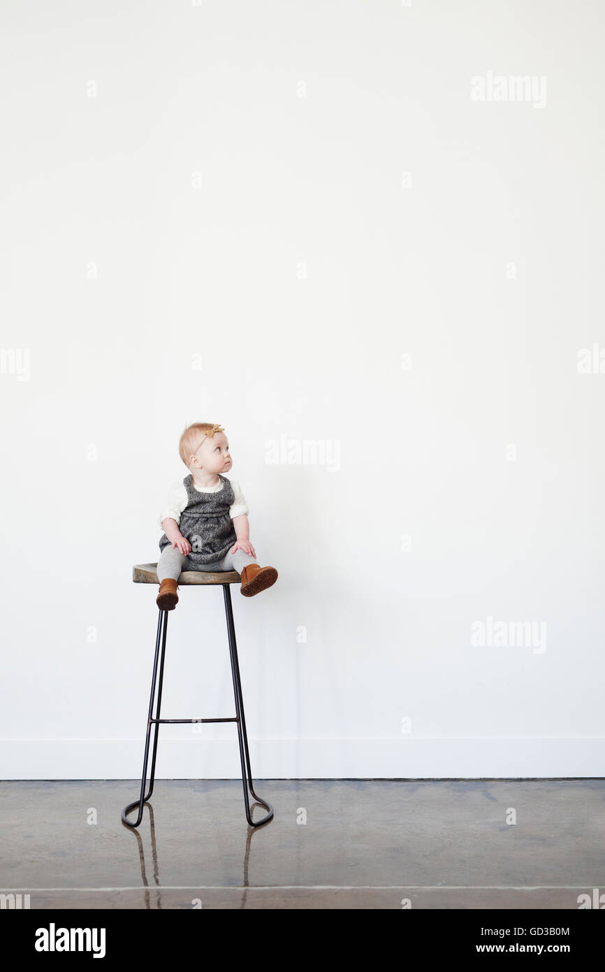 Un jeune enfant, une petite fille assise sur un grand tabouret. Banque D'Images