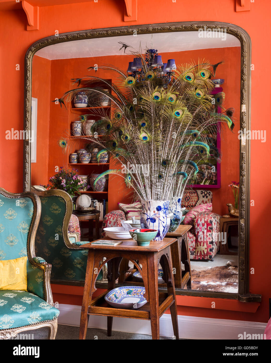 Vase de plumes de paon sur table en bois avec grand miroir en toile de fond. La pièce est peinte dans Charlotte's Locks par Farrow & Ball. Banque D'Images