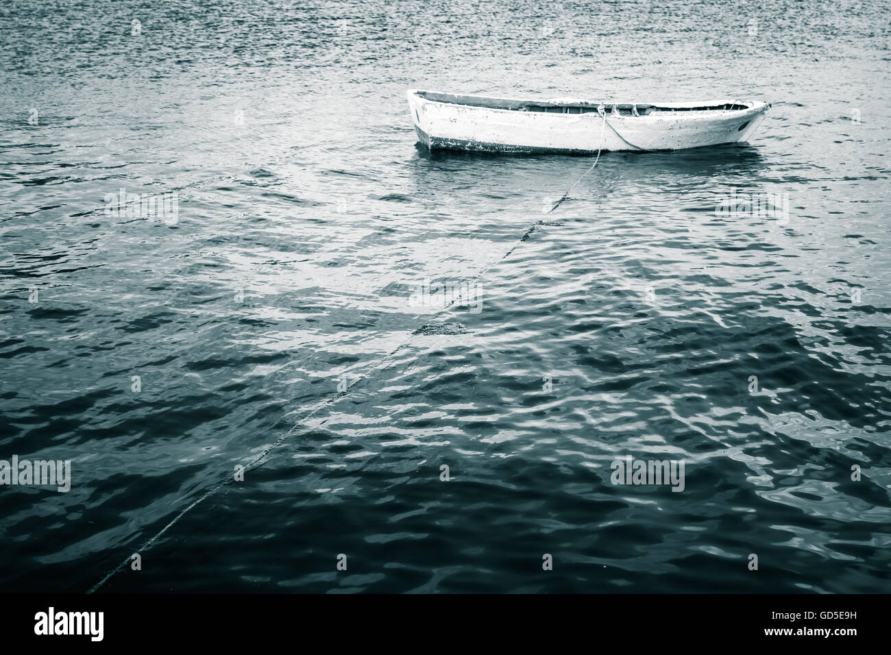 Bateau de pêche en bois blanc flotte sur la mer encore dans les tons bleus, vintage photo stylisée Banque D'Images
