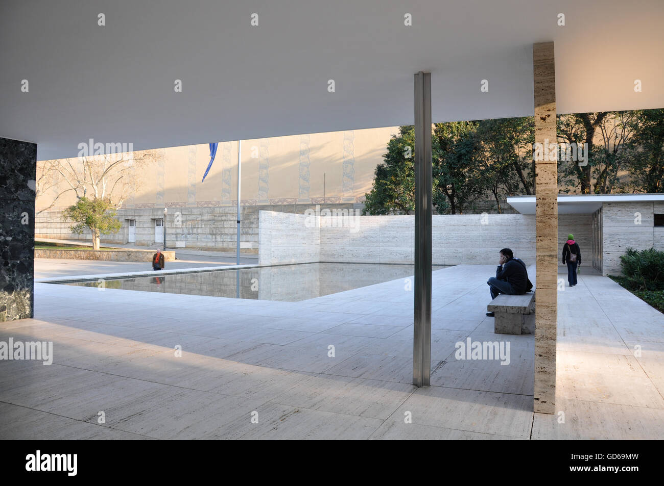 Miroir d'eau dans la construction géométrique avec l'homme assis sur le banc en pierre à proximité comme femme marche vers la sortie Banque D'Images