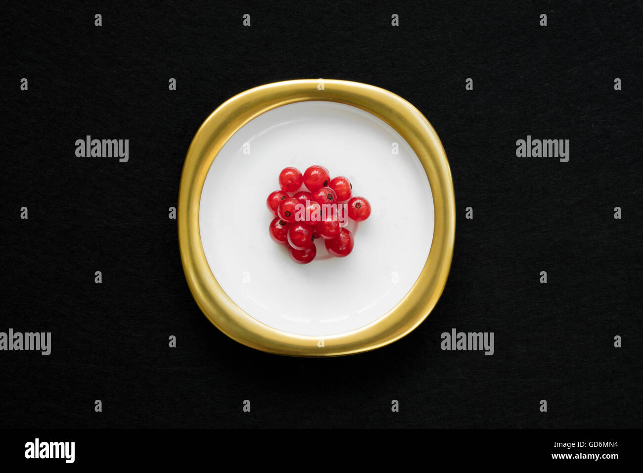 Groupe de groseille rouge placé sur un plat d'or avec fond noir isolé. Banque D'Images
