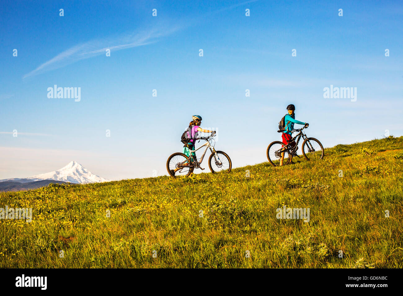 Deux jeunes femmes pousser les vélos de montagne d'un sentier à voie unique par le biais d'un pré. Banque D'Images