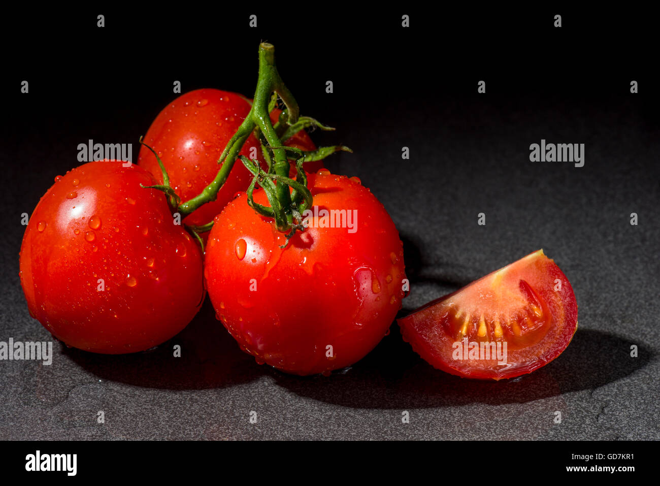 Trois tomates mûries sur vigne fraîche un fond noir. Banque D'Images