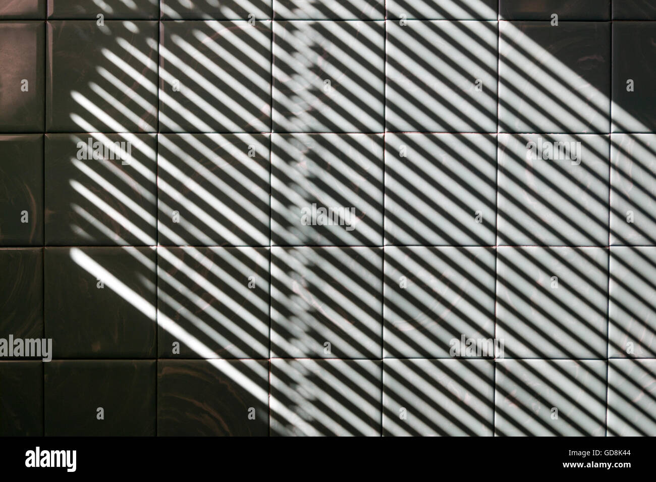 Le soleil qui rayonne à travers les stores vénitiens avec un motif d'ombre et de lumière sur un mur de carreaux de salle de bains Banque D'Images