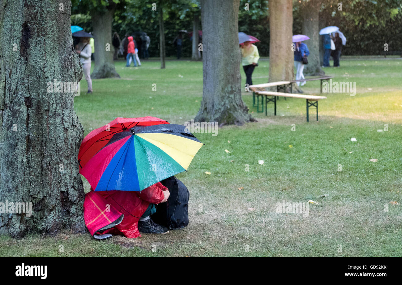 Hanovre, Allemagne. Le 13 juillet, 2016. Les visiteurs avec des parasols perchaude sous un arbre dans le jardins de Herrenhausen à la première de 'Kleines Fest im Grossen Garten" à Hanovre, Allemagne, 13 juillet 2016. Un orage avec des éclairs et tonnerre, pluie et tempête a provoqué la fin de la première soirée des arts festival. Photo : Julian Stratenschulte/dpa/Alamy Live News Banque D'Images