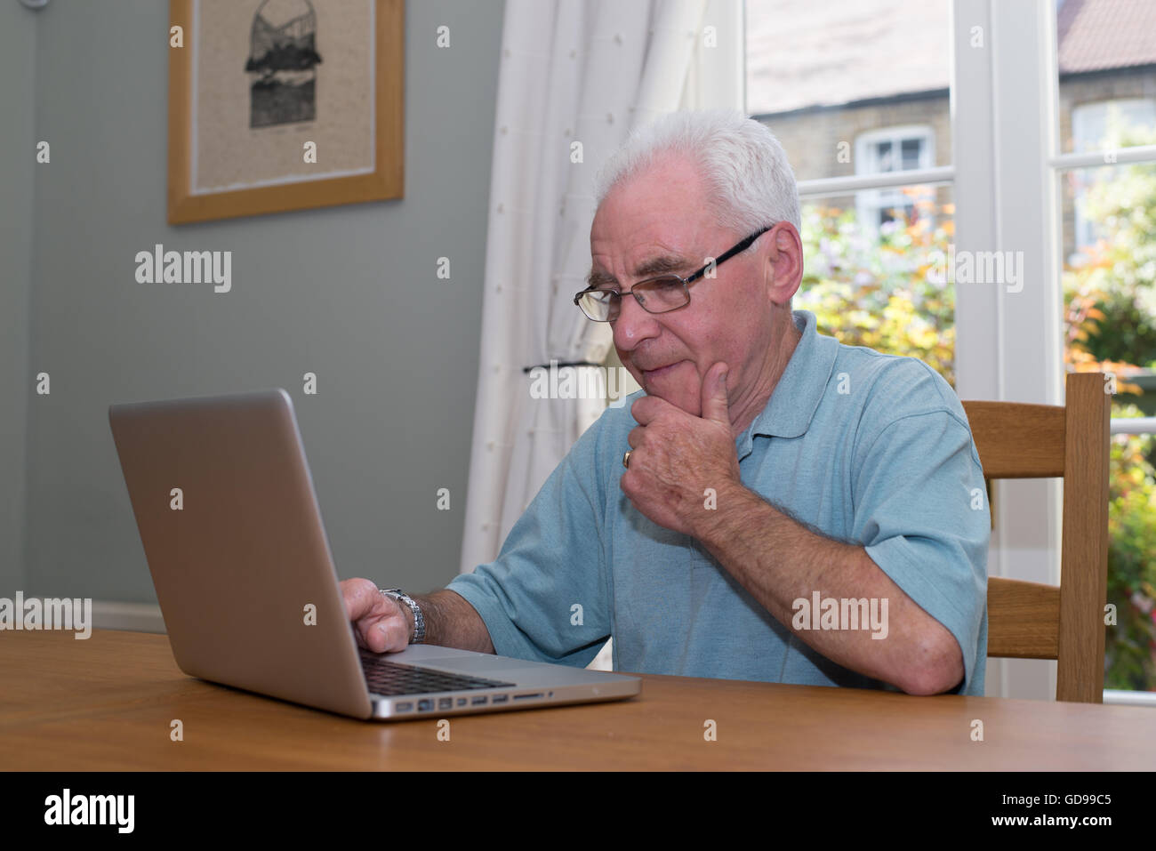 Vieil homme est assis à une table à l'aide d'un ordinateur portable Banque D'Images