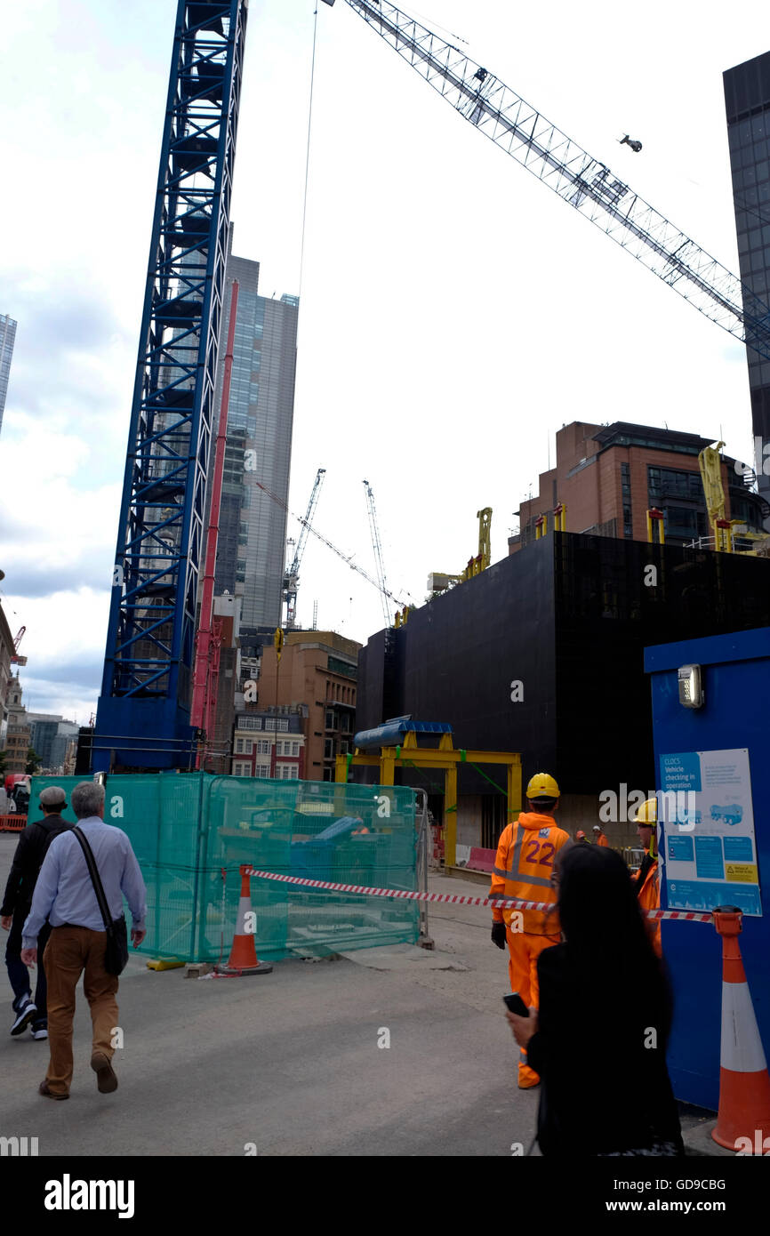 Un chantier avec les ouvriers en construction en salopette orange vif sur un chantier dans la ville de Londres de la CDB, les piétons à pied passé Banque D'Images