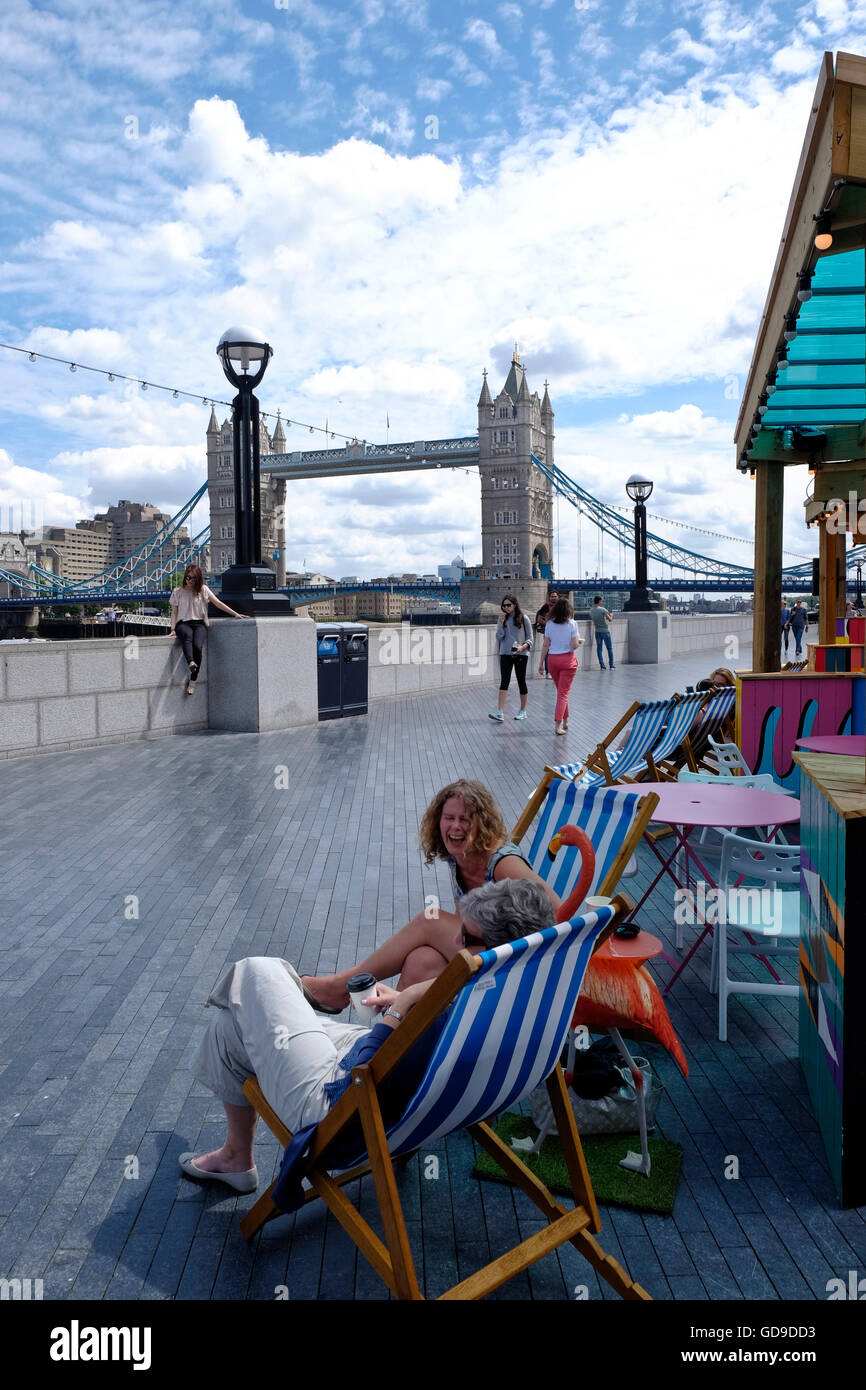 Les Londoniens vous détendre dans des chaises longues dans un restaurant situé sur la promenade le long de la Tamise Tower Bridge Londres un jalon dans l'arrière-plan Banque D'Images