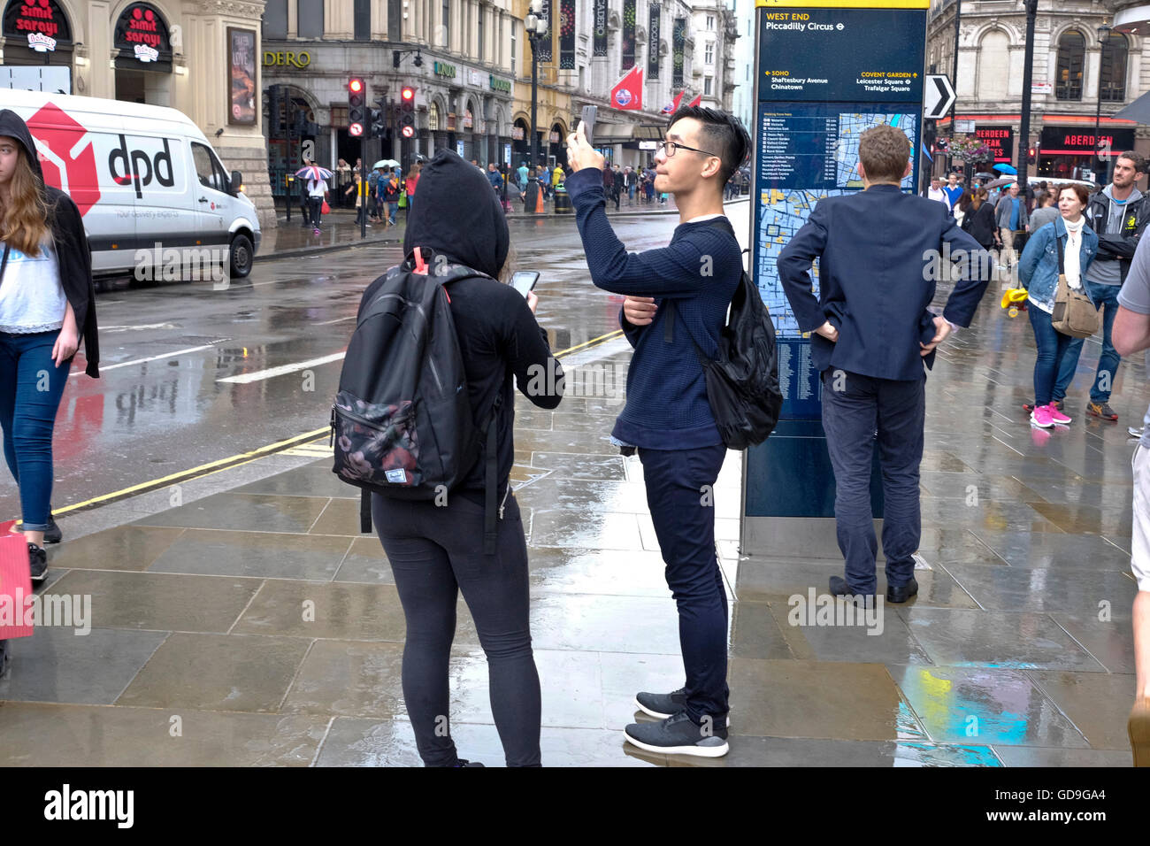 Piccadilly Circus Londres. Un touriste chinois prend une photo d'Eros avec son téléphone intelligent à l'état humide et pluvieux jour dans Piccadilly Circus Londres Banque D'Images