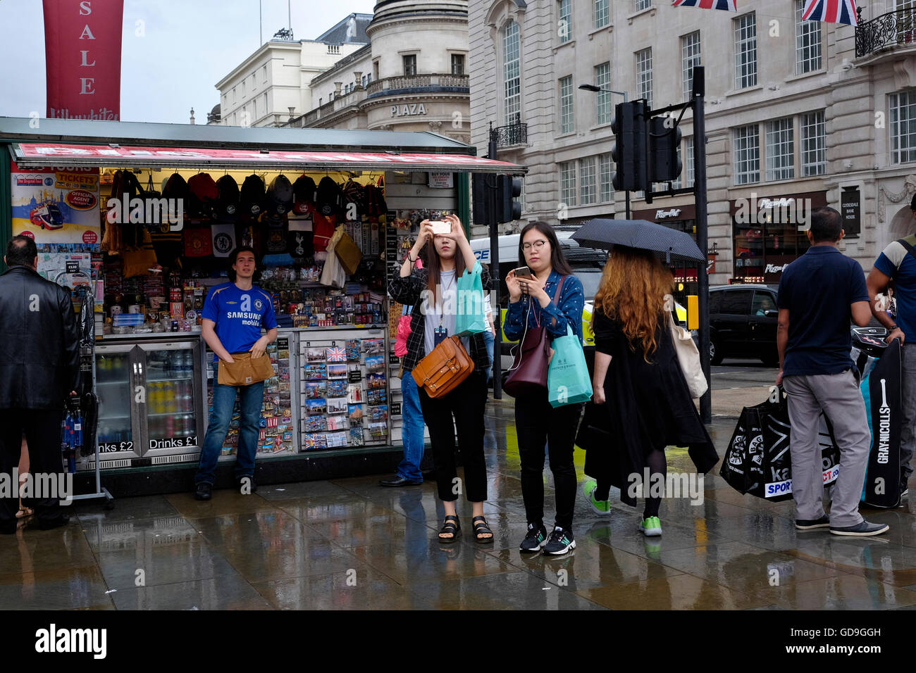 London Piccadilly Circus. Les touristes prenant des photos debout devant un stand de vendeurs de bibelots sur un jour de pluie. Banque D'Images