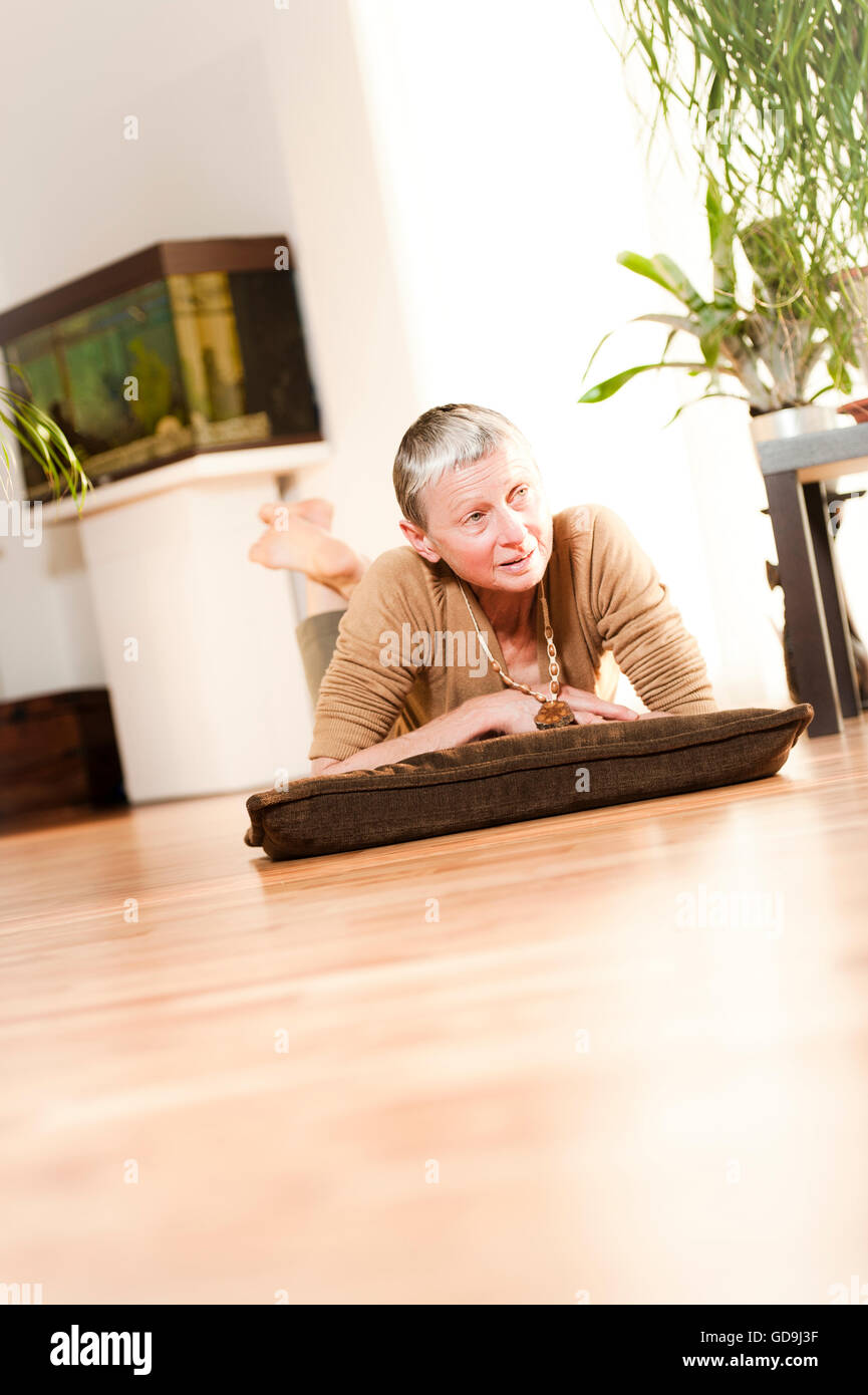 Femme, 60 +, le mensonge, la détente sur le plancher dans la salle de séjour Banque D'Images