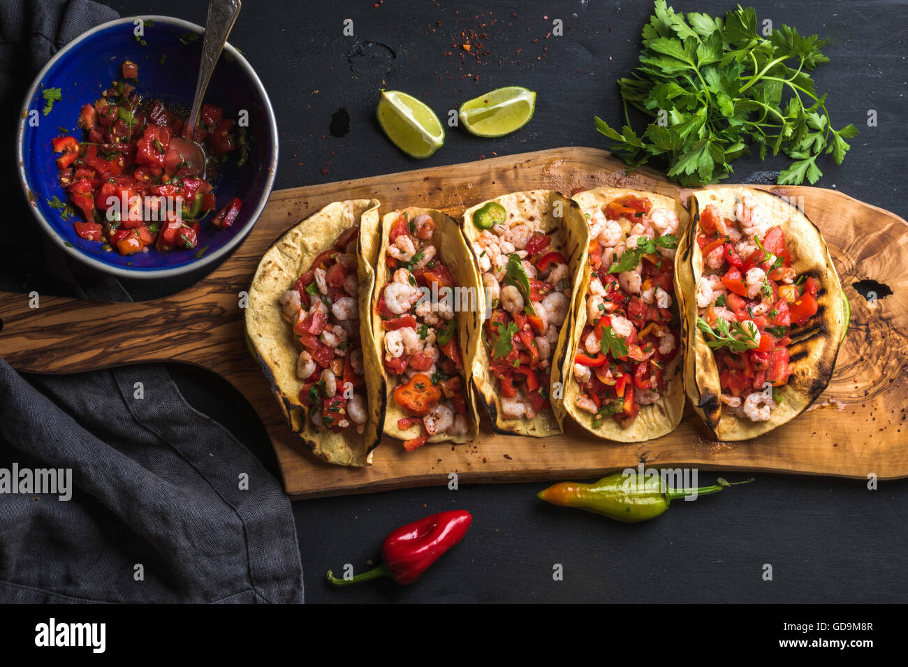 Tacos de crevettes avec sauce salsa maison, limes et le persil sur planche de bois sur fond sombre. Vue d'en haut. La cuisine mexicaine Banque D'Images