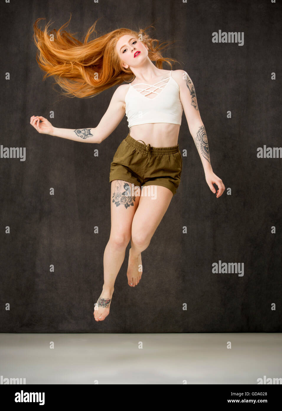 Jeune femme aux longs cheveux rouges et des tatouages portant des shorts vert et le saut avec cheveu qui coule derrière. Banque D'Images