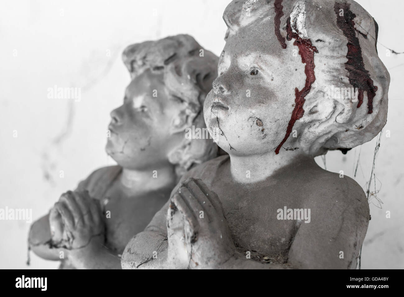 Statue d'un enfant priant, couverts de toiles d'araignée et le sang séché. Arrière-plan flou flou artistique. Banque D'Images