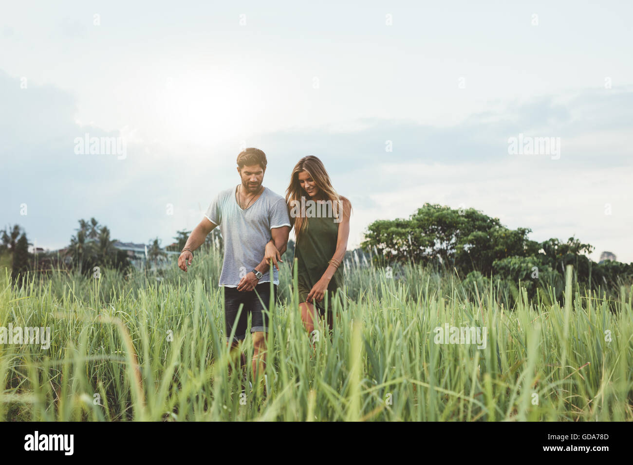Piscine shot of young couple walking through grass field. L'homme et la femme marche dans la nature. Banque D'Images