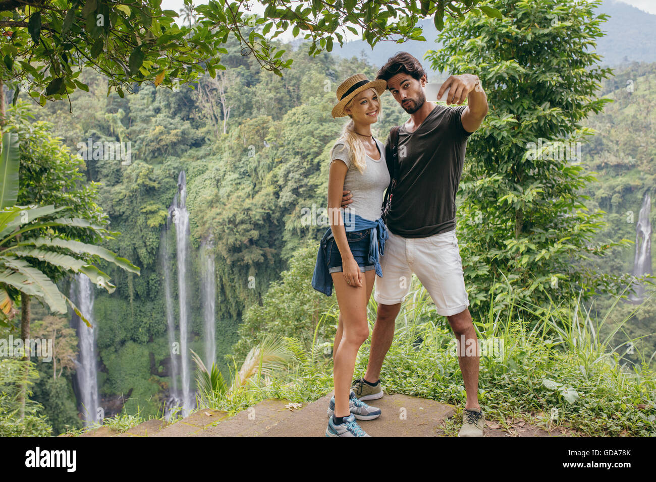 Belle jeune couple sur une falaise et en tenant avec cascade. selfies L'homme et de la femme dans la forêt prendre des auto portra Banque D'Images
