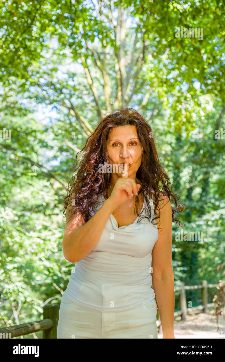 Femme mature chic en courbes, mettre l'index sur les lèvres pour garder le silence dans un jardin Banque D'Images
