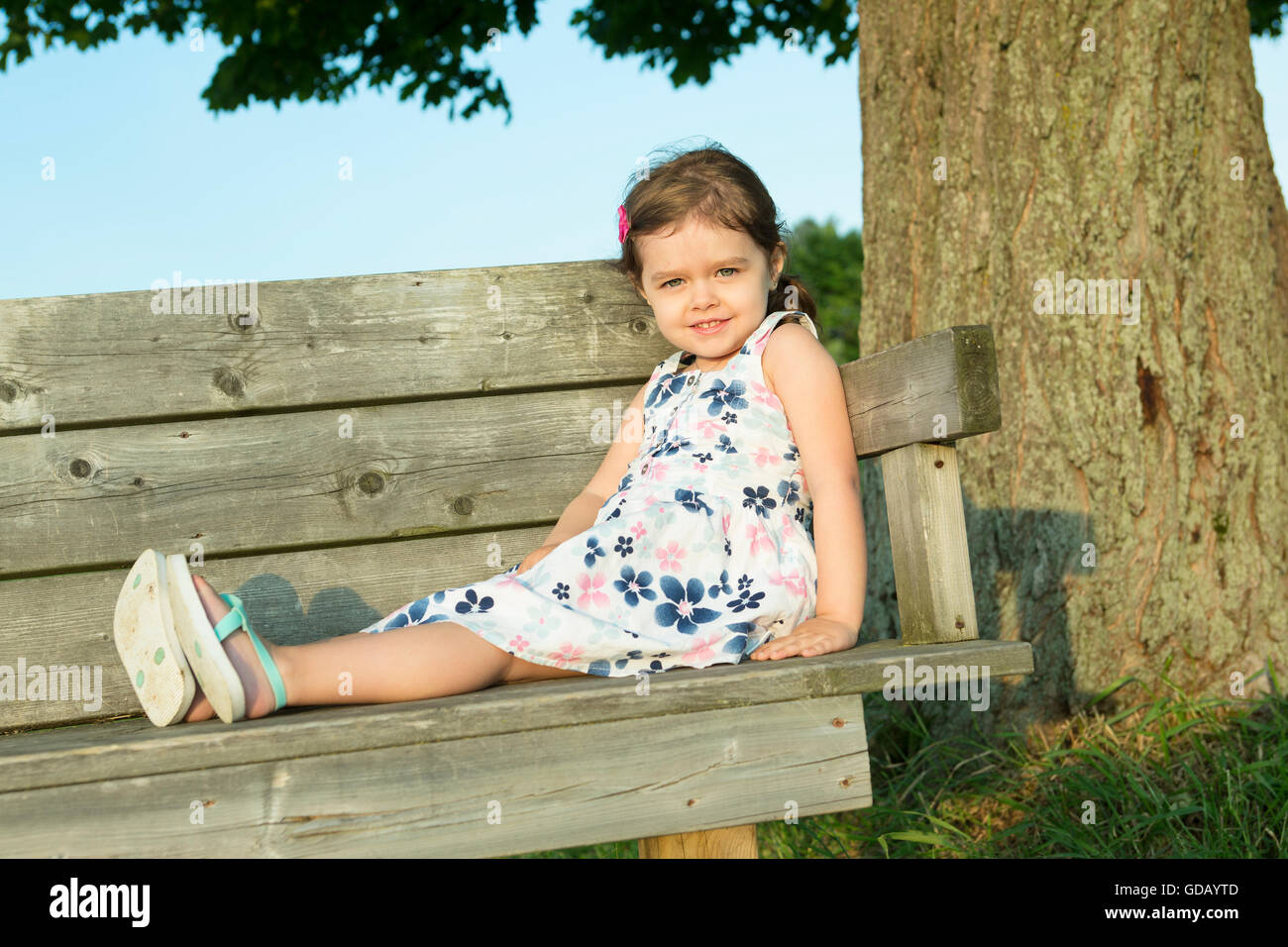 Happy cute petite fille assise sur un banc Banque D'Images