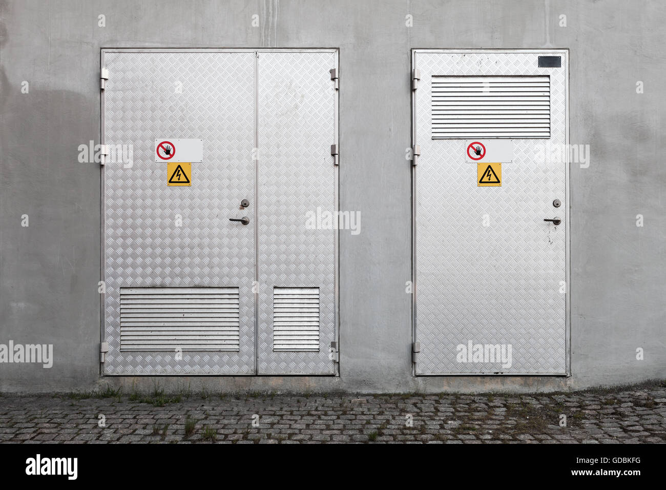 Les portes métalliques avec des panneaux d'avertissement de tension élevée dans l'industrie de béton gris, texture mur de fond photo, vue de face Banque D'Images