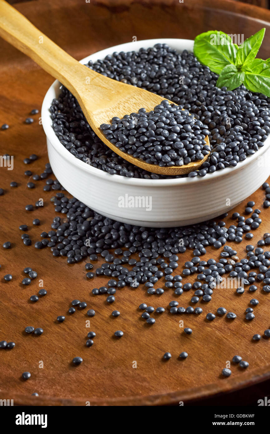 Bol blanc rond plein de lentilles béluga et les feuilles de basilic avec une cuillère de bois sur fond de bois brun. Banque D'Images