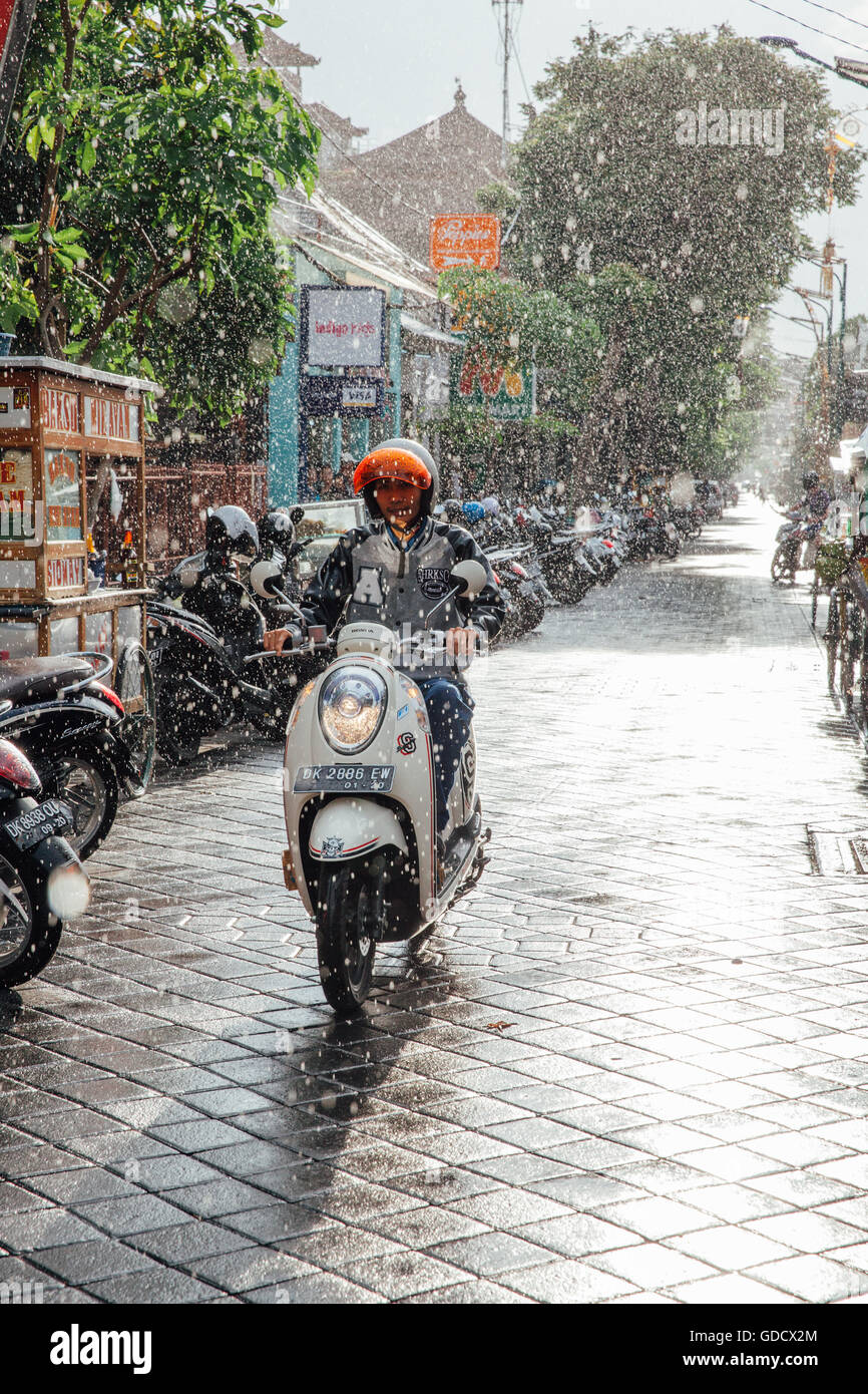 Indonesian man riding une moto sous la pluie sur la rue de Kuta, Bali, Indonésie. Banque D'Images