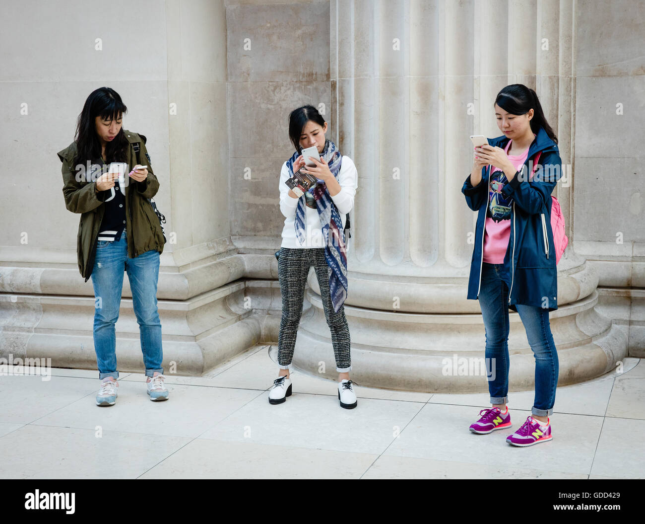 Trois amis asiatiques dans le British Museum de Londres Royaume-uni étudier attentivement leurs téléphones intelligents Banque D'Images