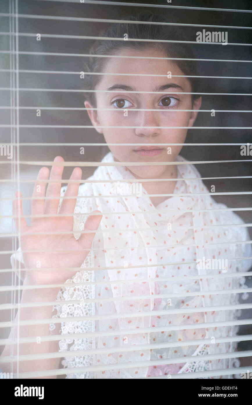 Girl looking through blinds perse sur la fenêtre Banque D'Images