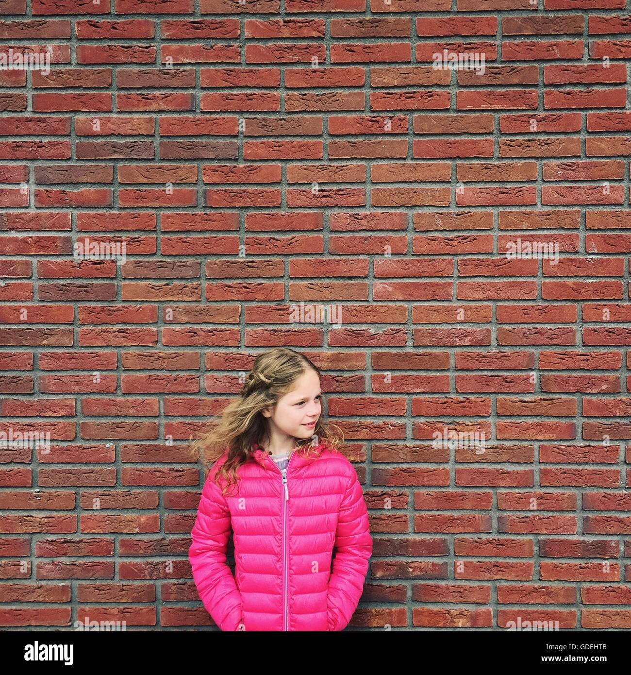 Portrait of Girl in pink jacket standing against brick wall Banque D'Images