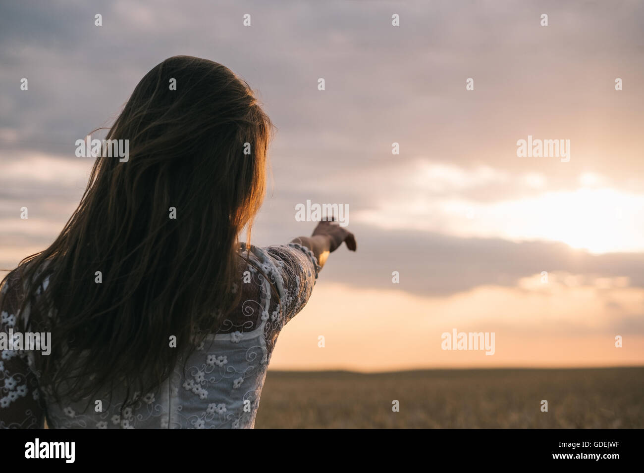Femme debout dans un champ de blé vers le coucher du soleil Banque D'Images