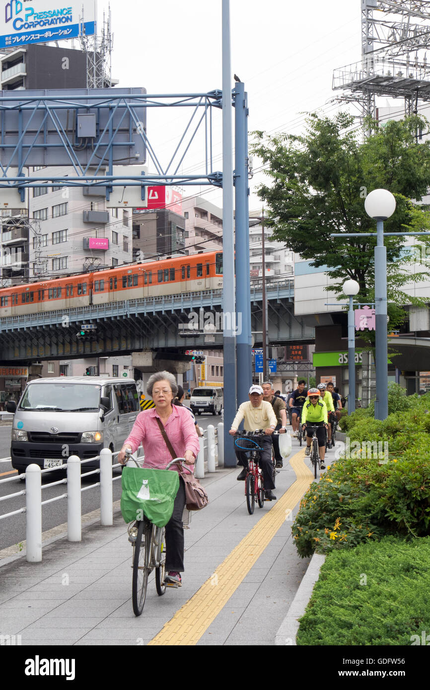 Deux cyclistes vélo parmi les locaux dans le centre d'Osaka. Banque D'Images