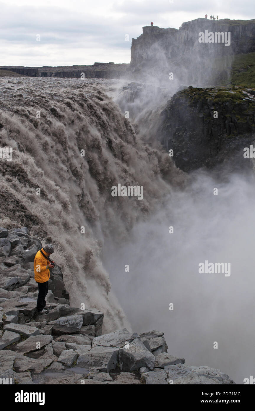 Islande : un homme avec un imperméable jaune prendre des photos de Dettifoss, l'une des plus puissantes en cascade l'Europe, célèbre pour ses paysages exotiques Banque D'Images