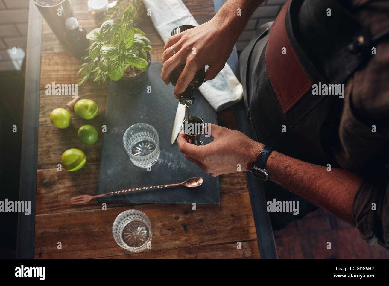 Close up de mains barman pouring alcoholic drink dans d'une turlutte de préparer un cocktail, avec des feuilles de basilic et les citrons sur le bar c Banque D'Images