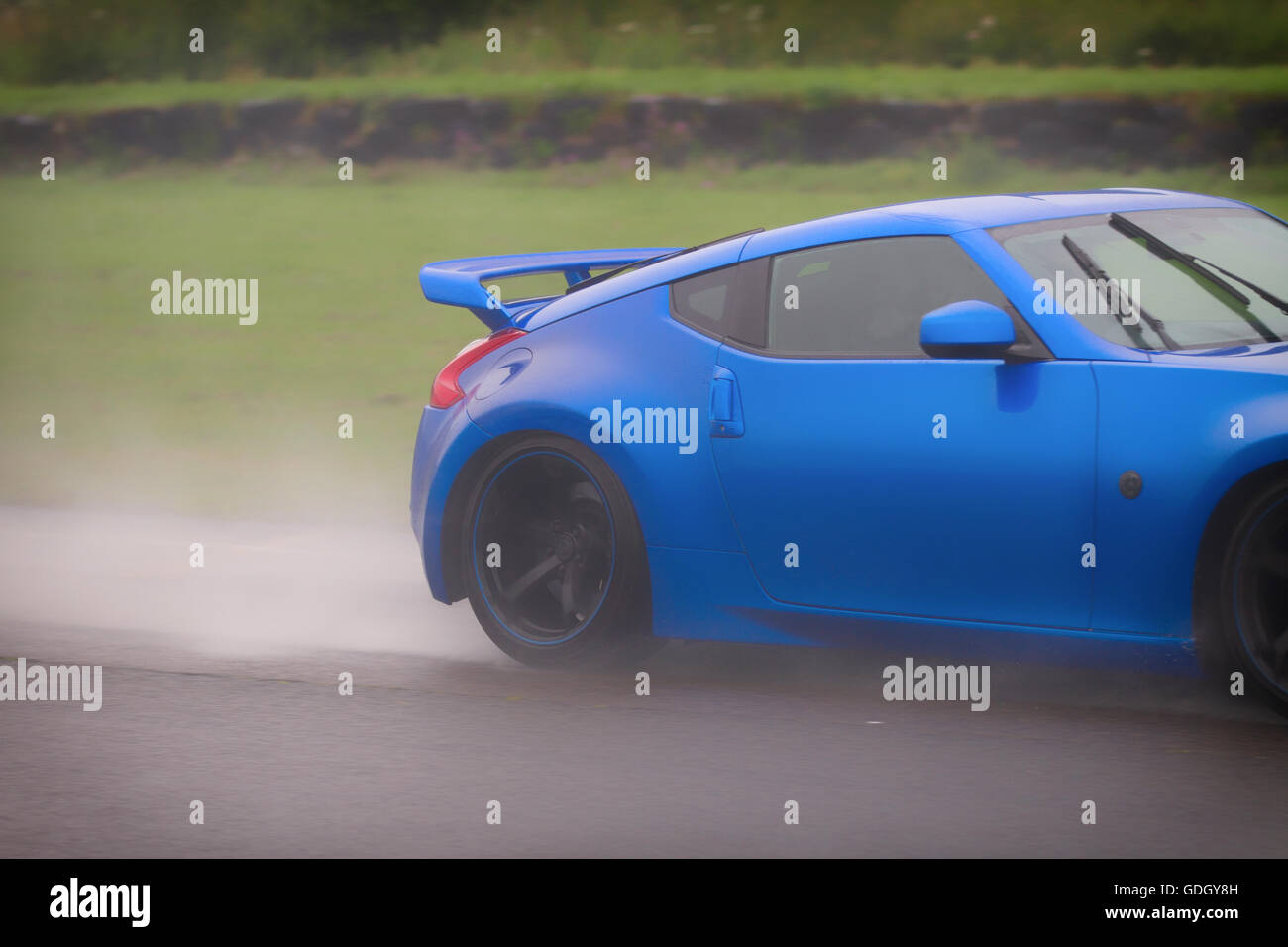 Speedy blue voiture rapide dans un jet d'eau de pluie et brouillard se déplaçant à grande vitesse sur une route mouillée. Banque D'Images