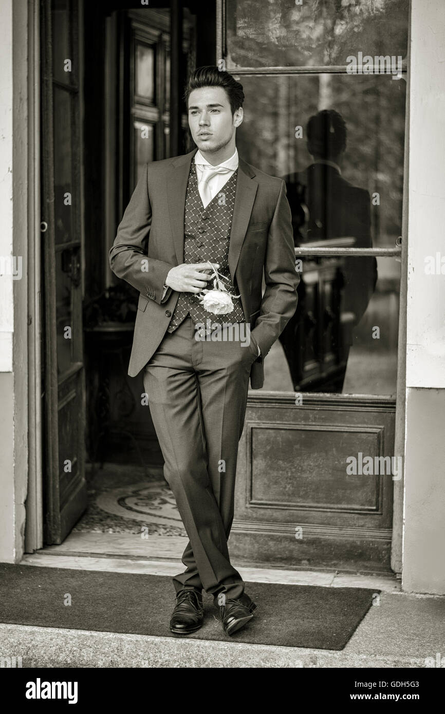 Portrait du jeune élégant costume gris en bridgegroom maintenant fleur blanche. Beau jeune homme en costume sombre attend sa femme Banque D'Images