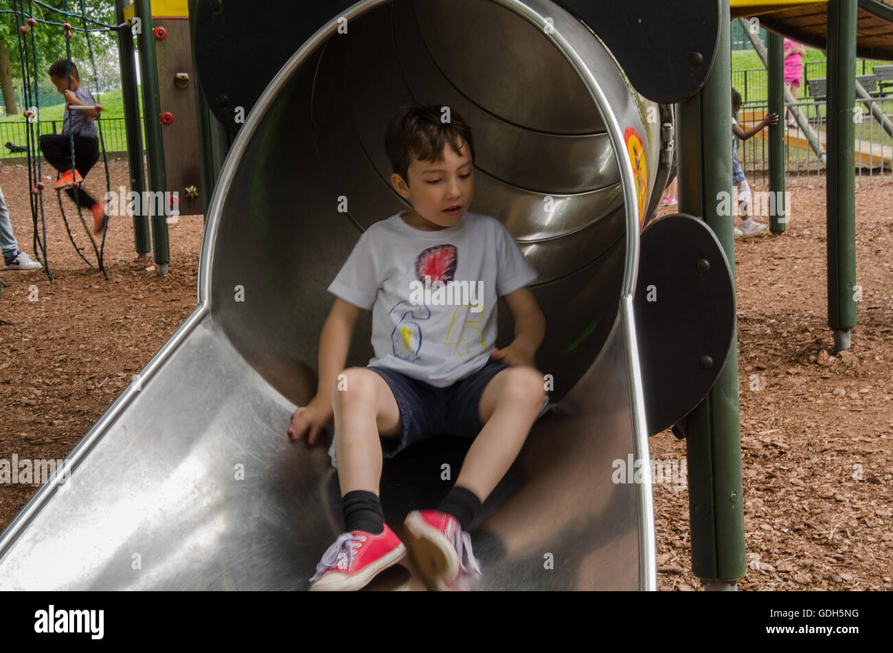 Un jeune garçon apparaît au bas de la diapositive dans une aire de jeux pour enfants dans la région de Prospect Park, lecture. Banque D'Images