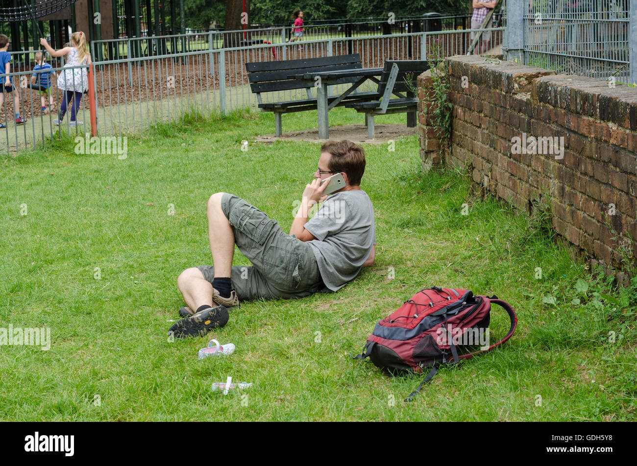 Un homme se détend sur un patch d'herbe dans le parc tout en prenant un appel téléphonique sur son téléphone mobile. Banque D'Images
