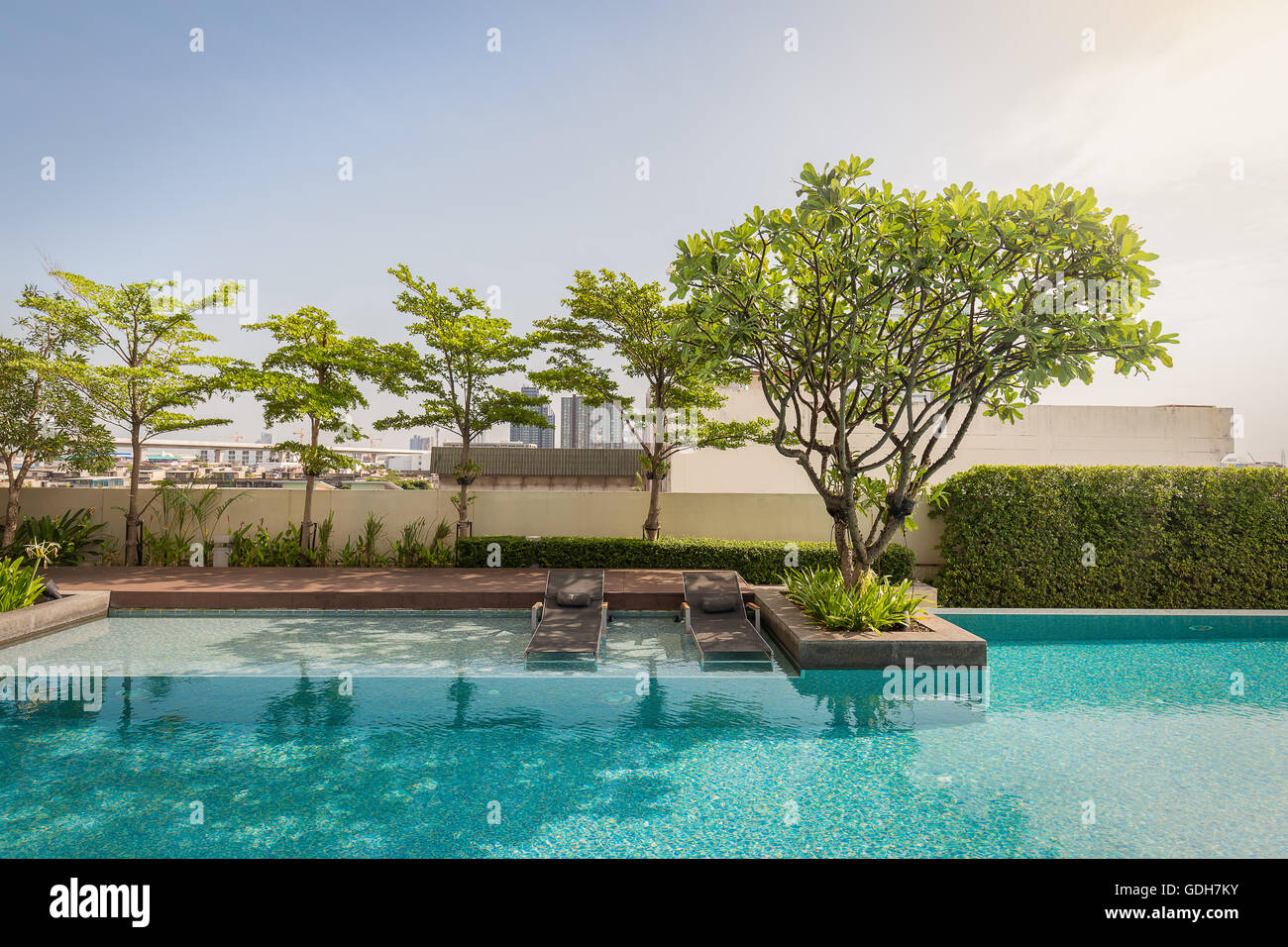 Deux banc de plage sous l'ombre des arbres sur la base de pas en bas de la mosaïque piscine qui entoure d'arbres et de bush. Banque D'Images