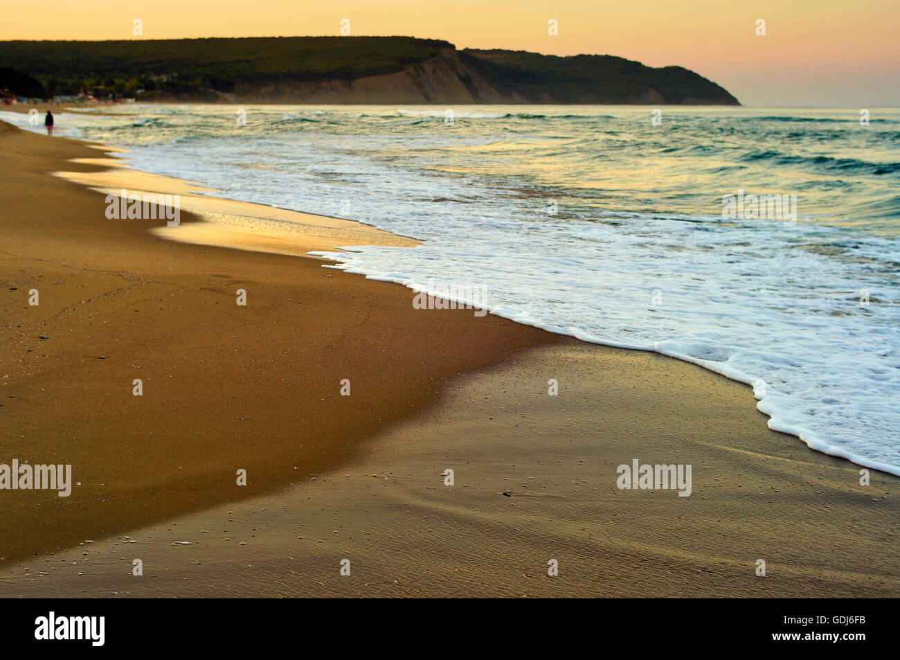 Personne qui marche au loin sur une plage de sable sauvage sous la lumière dorée d'un soir d'été. Banque D'Images