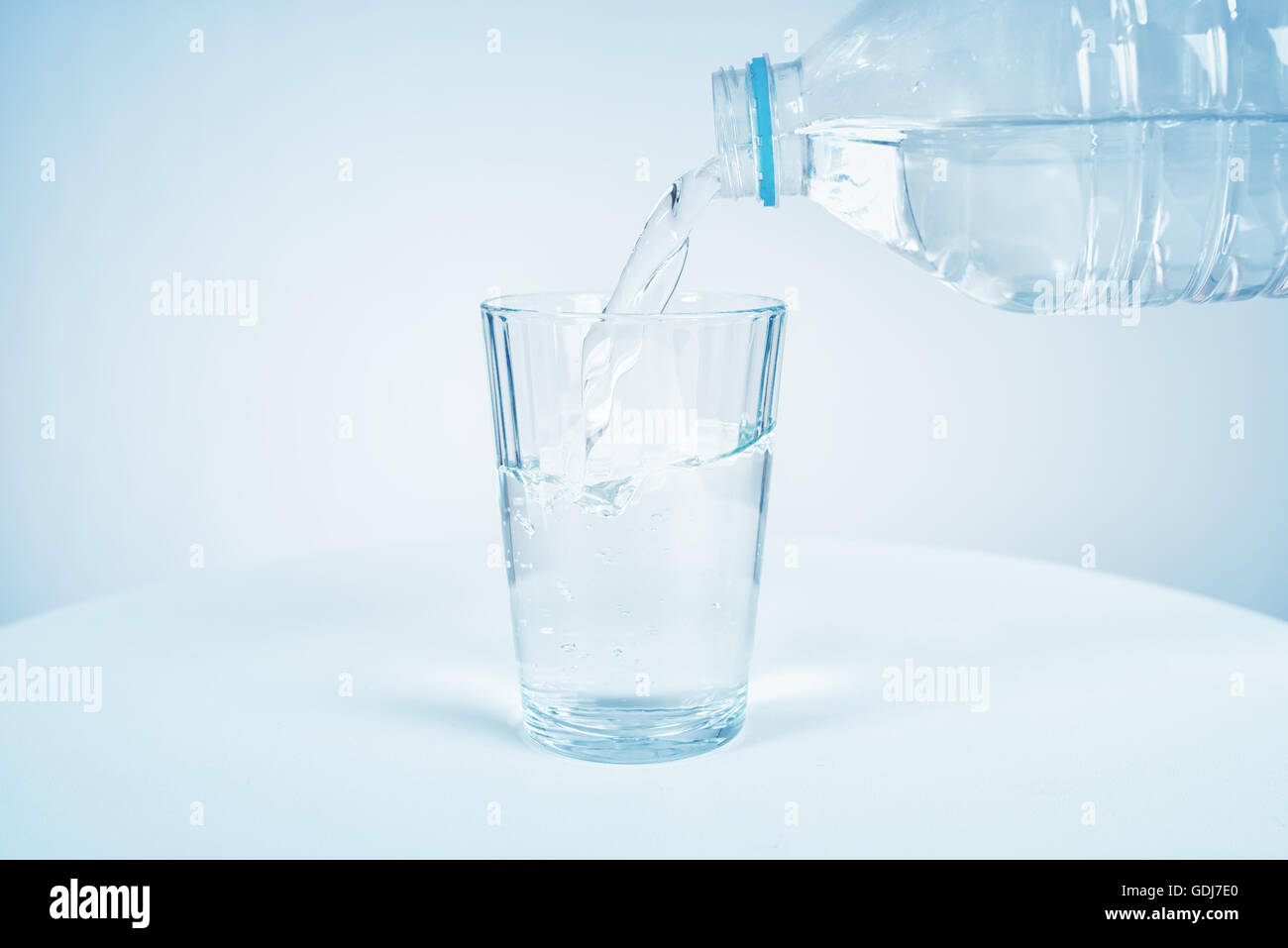 Verser de l'eau de la bouteille en verre sur fond bleu Banque D'Images