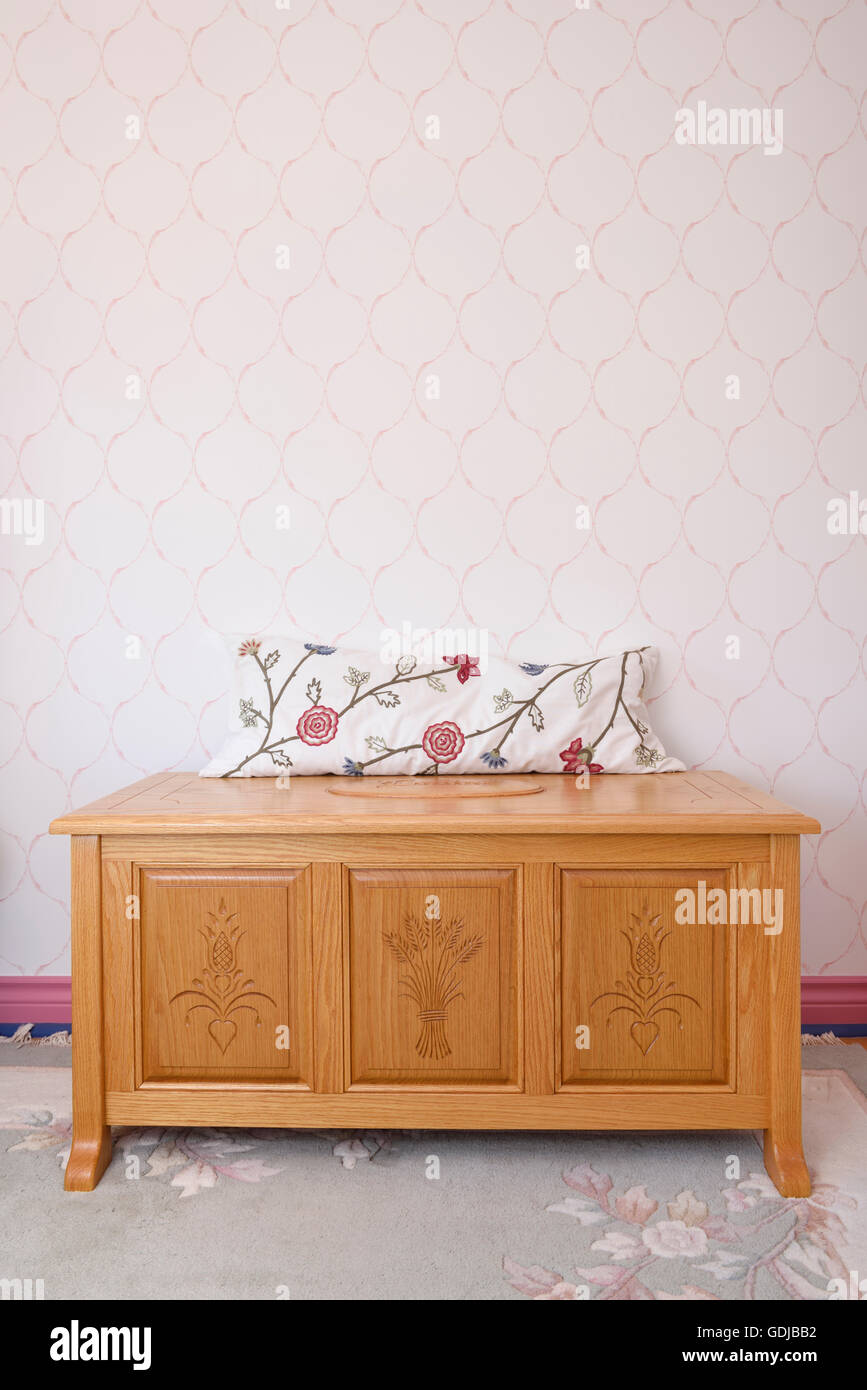 En chêne sculpté main coffre de cèdre avec oreiller dans la chambre avec du papier peint rose Banque D'Images