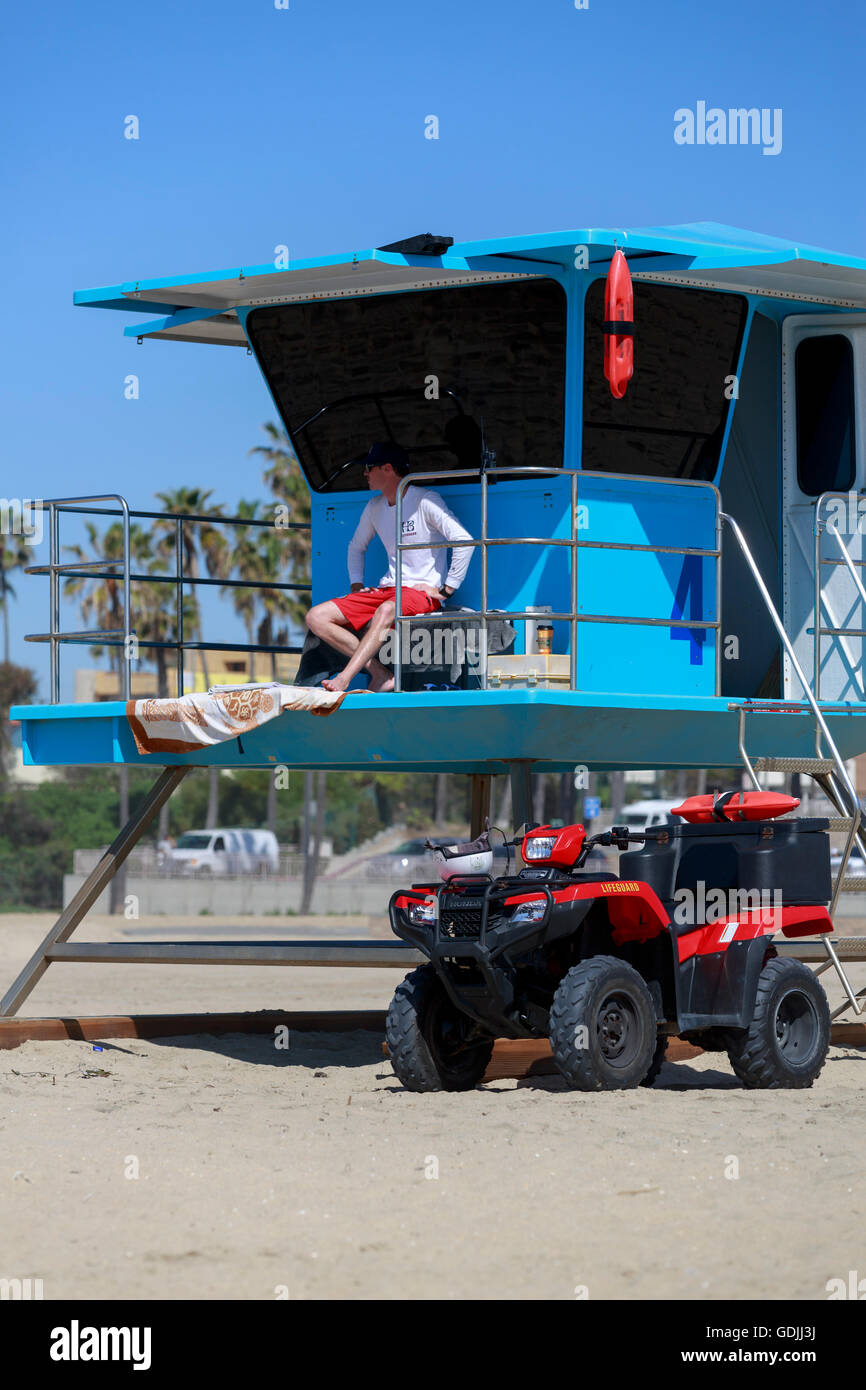 Peint bleu lifeguard poste numéro 4 avec Huntigton Beach lifeguard assis attentivement et sa Honda ATV garé ci-dessous Banque D'Images
