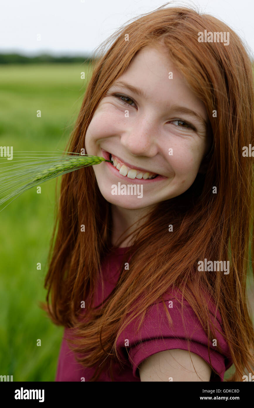 Smiling teenage girl, rire, avec l'orge en herbe dans sa bouche, Allemagne Banque D'Images