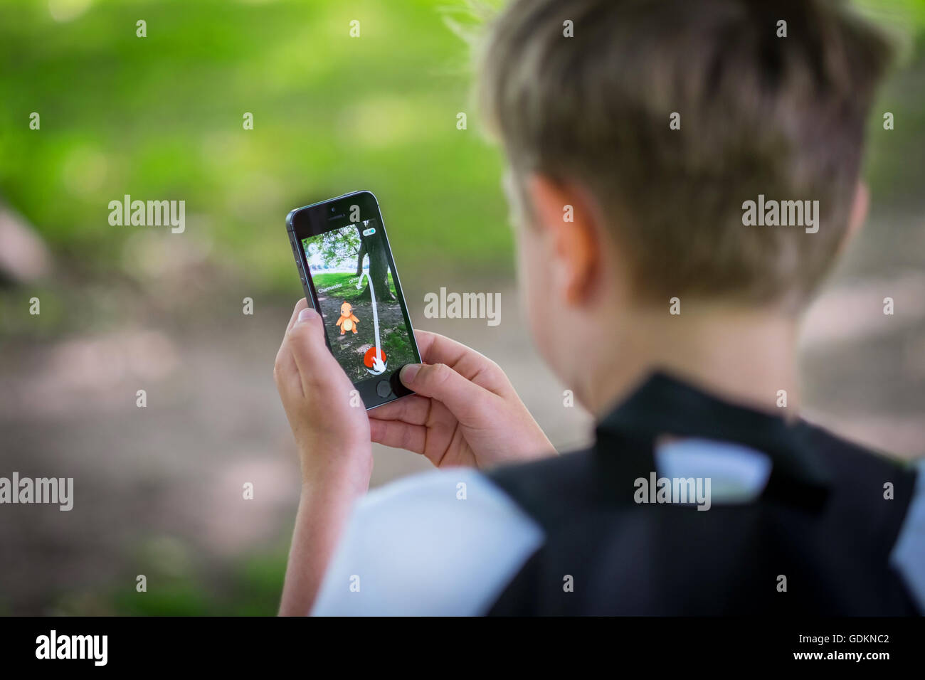 Un garçon dans le parc et jouent le nouveau Pokemon le jeu de Go sur son téléphone Banque D'Images