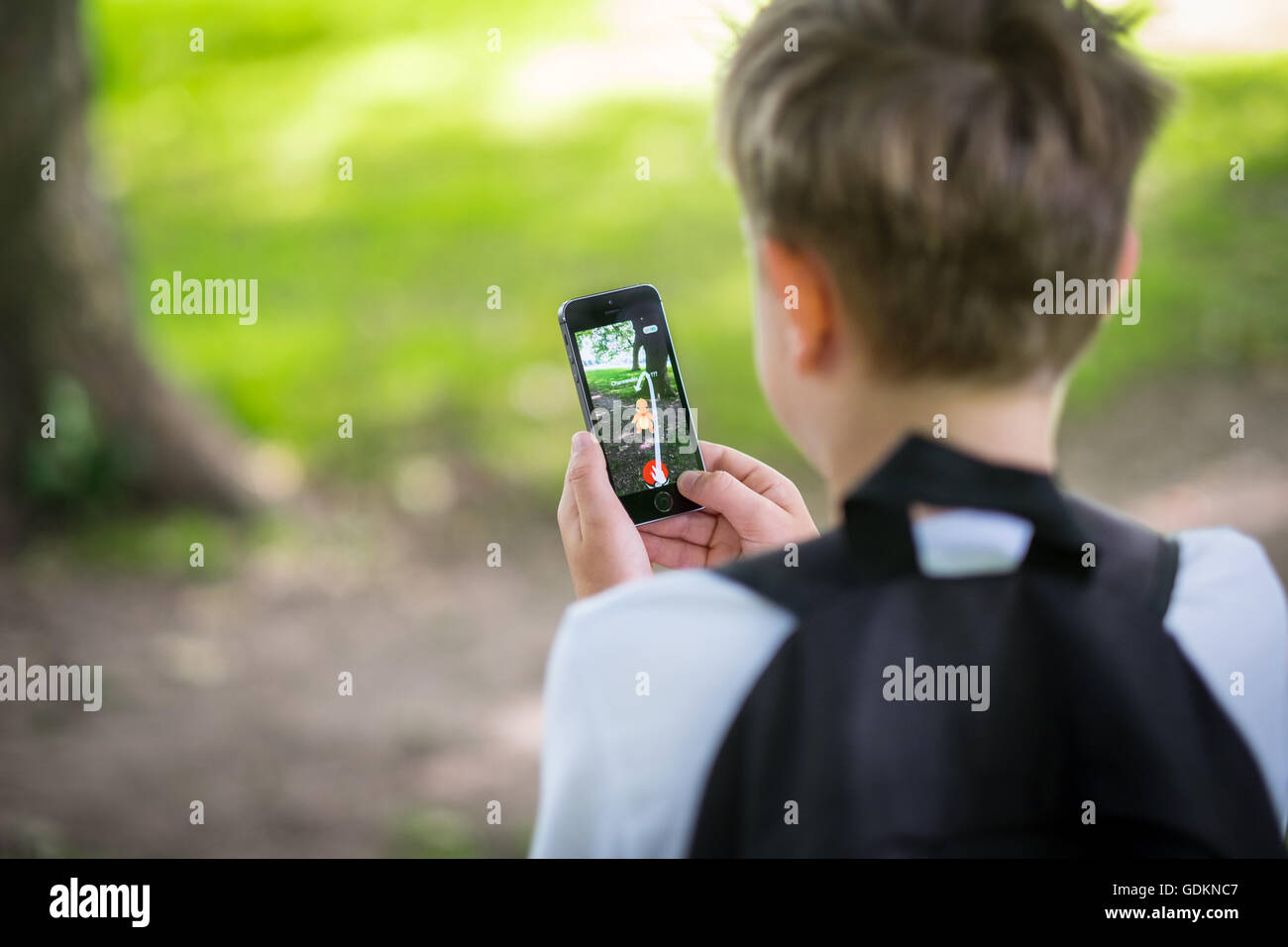 Un garçon dans le parc et jouent le nouveau Pokemon le jeu de Go sur son téléphone Banque D'Images