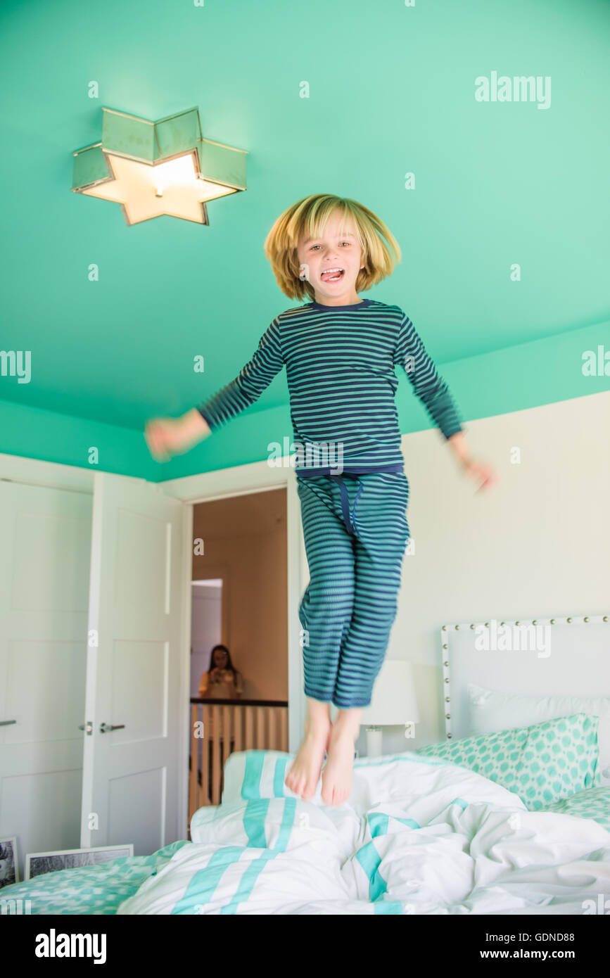 Boy wearing pajamas jumping on bed smiling Banque D'Images