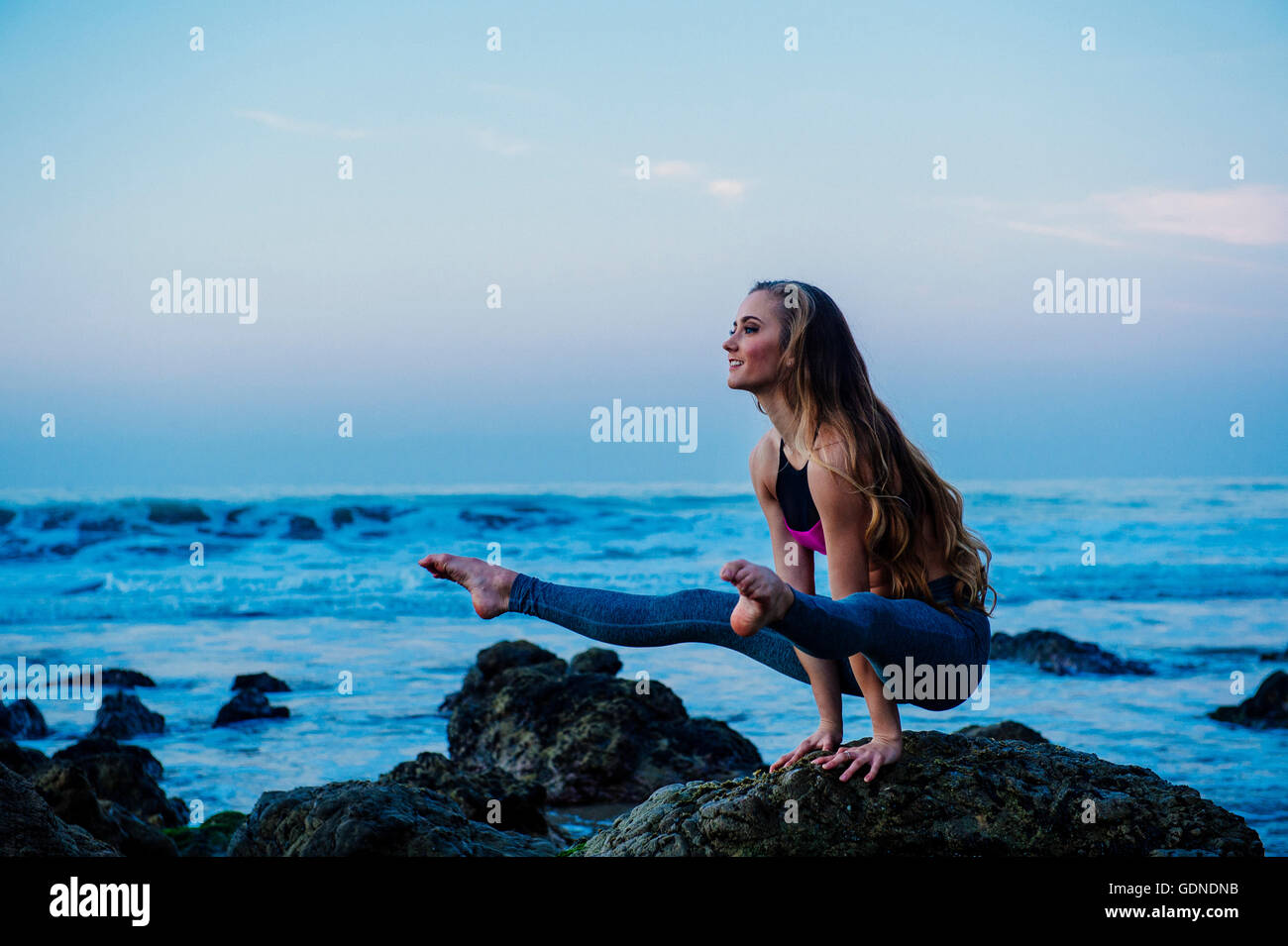 Young woman practicing yoga pose sur des roches en beach, Los Angeles, Californie, USA Banque D'Images