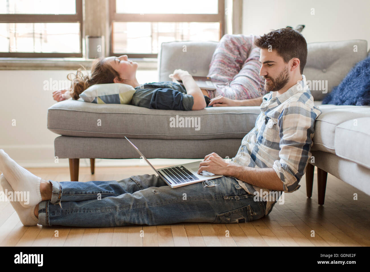 Young couple relaxing at home, jeune femme dormant sur un canapé, young man using laptop Banque D'Images