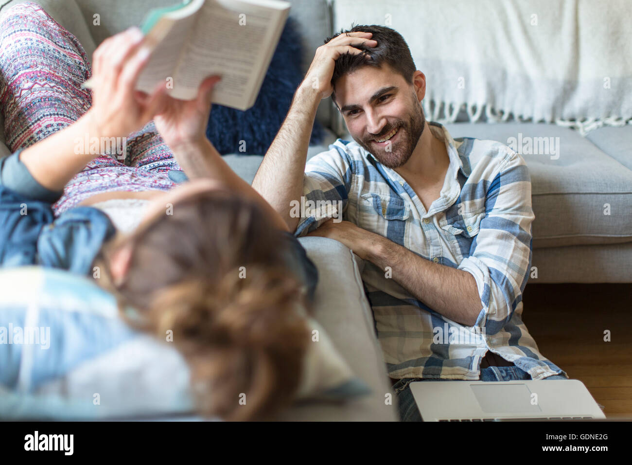 Young couple relaxing at home, young woman lying on sofa, young man sitting on floor, rire Banque D'Images