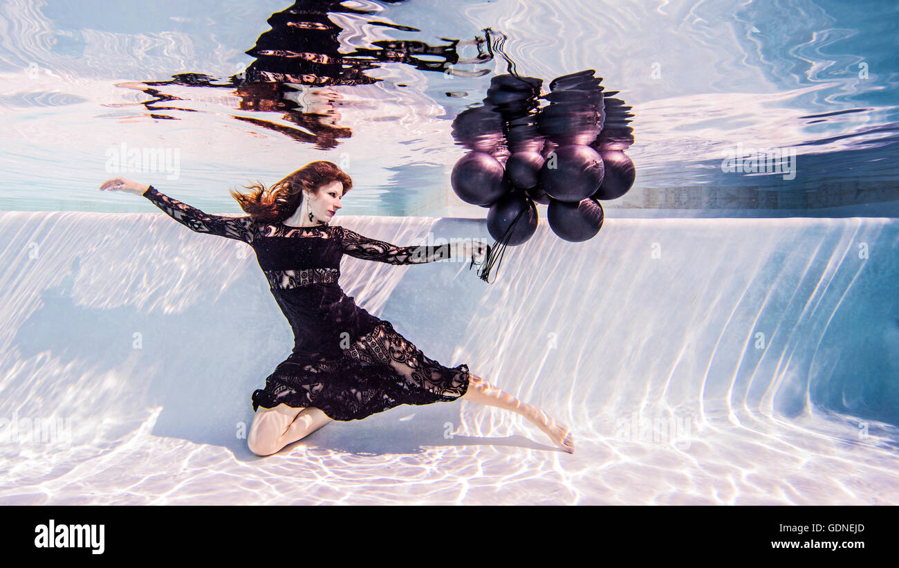 Woman wearing dress sous l'eau à la piscine holding bunch of balloons Banque D'Images