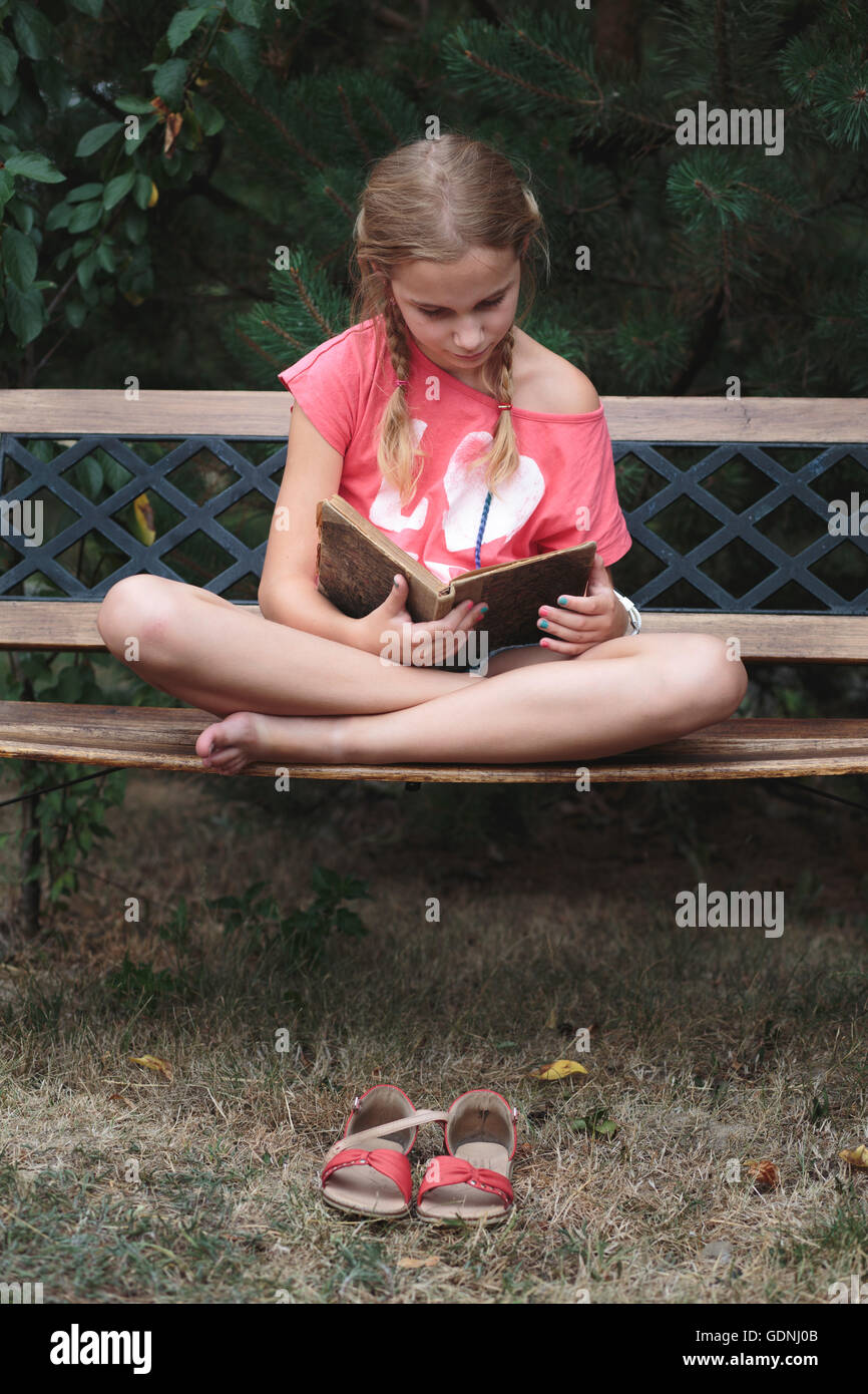 Jeune fille lisant un livre sur un banc dans le parc Banque D'Images